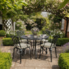 Outdoor garden setting with a round table and chairs surrounded by greenery and flowers.