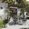 Outdoor patio setting with a round table and chairs, surrounded by plants and a pergola.