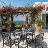 Outdoor patio set with table and chairs under a floral archway, overlooking the ocean.