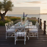 Outdoor dining setup with table and chairs by a body of water during sunset.
