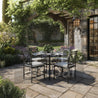 Outdoor patio set with table and chairs on a stone patio in a garden setting.