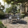 Outdoor patio set with table and chairs on a stone patio with garden and building in the background