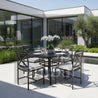 Outdoor dining set with table and chairs on a patio in front of a modern house.