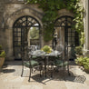 Outdoor patio setting with a round table and chairs in front of a stone building with arched windows.