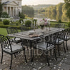 Outdoor dining set with table and chairs on a patio, featuring a scenic background with a house and lake.