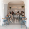 Shark Masa Takımı – Bohem ve Endüstriyel Cafeler İçin Katlanabilir Tasarım Mobilya - People sitting at tables in an organicly designed cave-like cafe with white walls and blue chairs.
