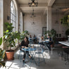Shark Masa Takımı – Bohem ve Endüstriyel Cafeler İçin Katlanabilir Tasarım Mobilya - People sitting at tables in a modern cafe with large windows and plants.