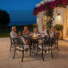 Group of people sitting around a fire pit table on a patio at night.